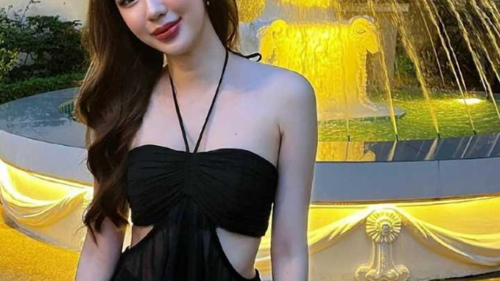 Woman in a black and blue dress poses near a fountain.