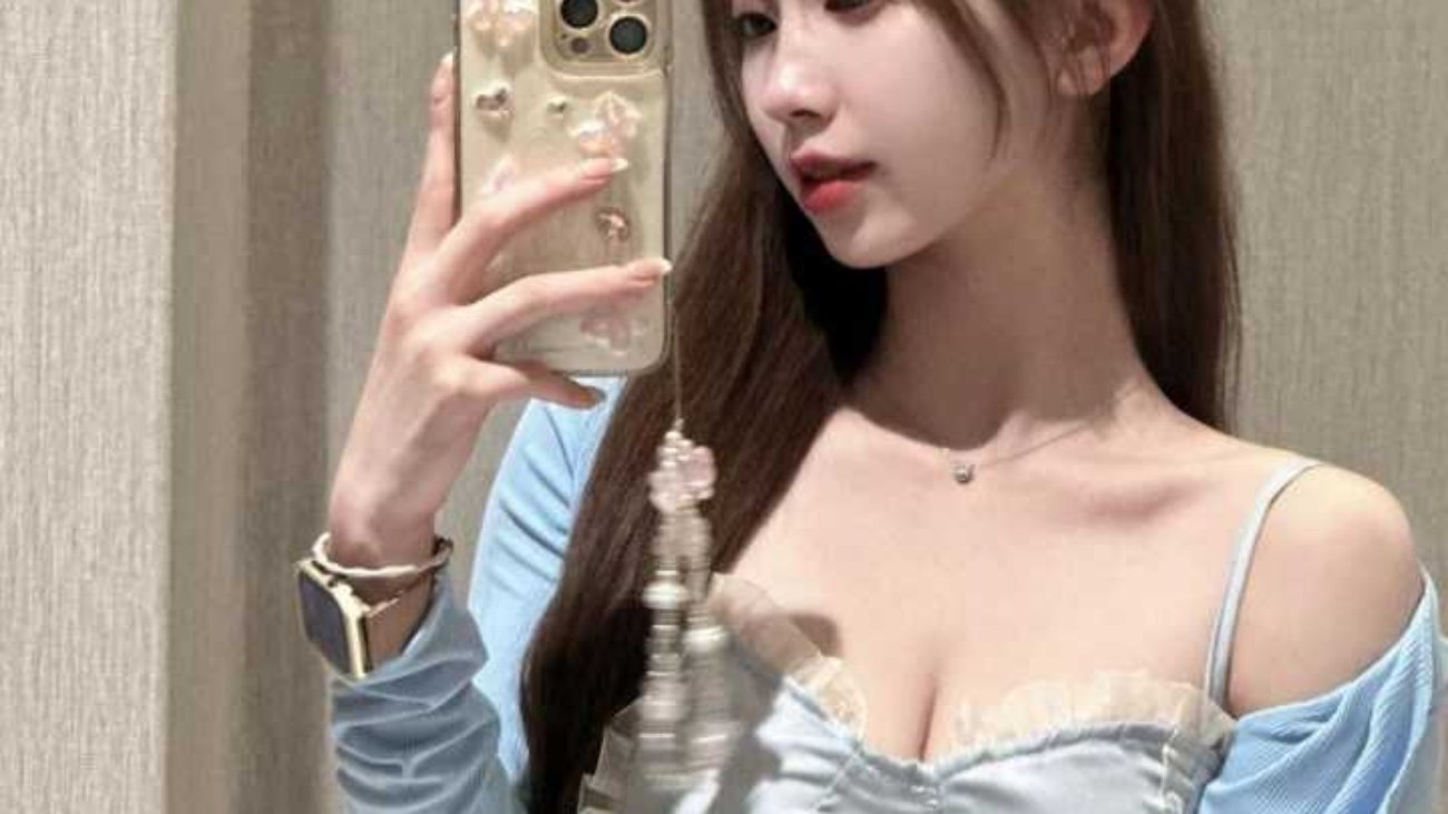 Woman taking a selfie in a light blue cardigan and skirt.