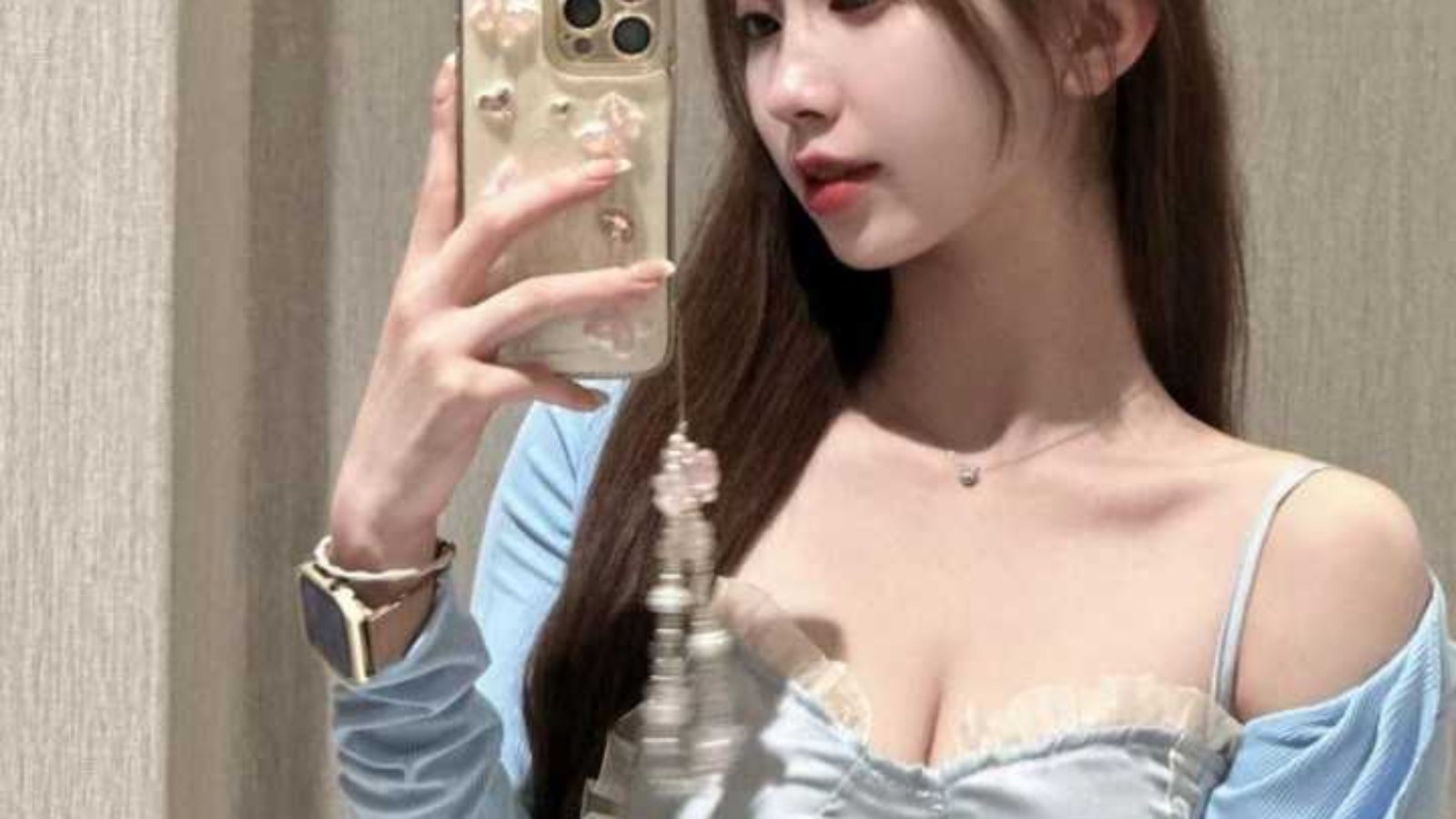 Woman taking a selfie in a light blue cardigan and skirt.