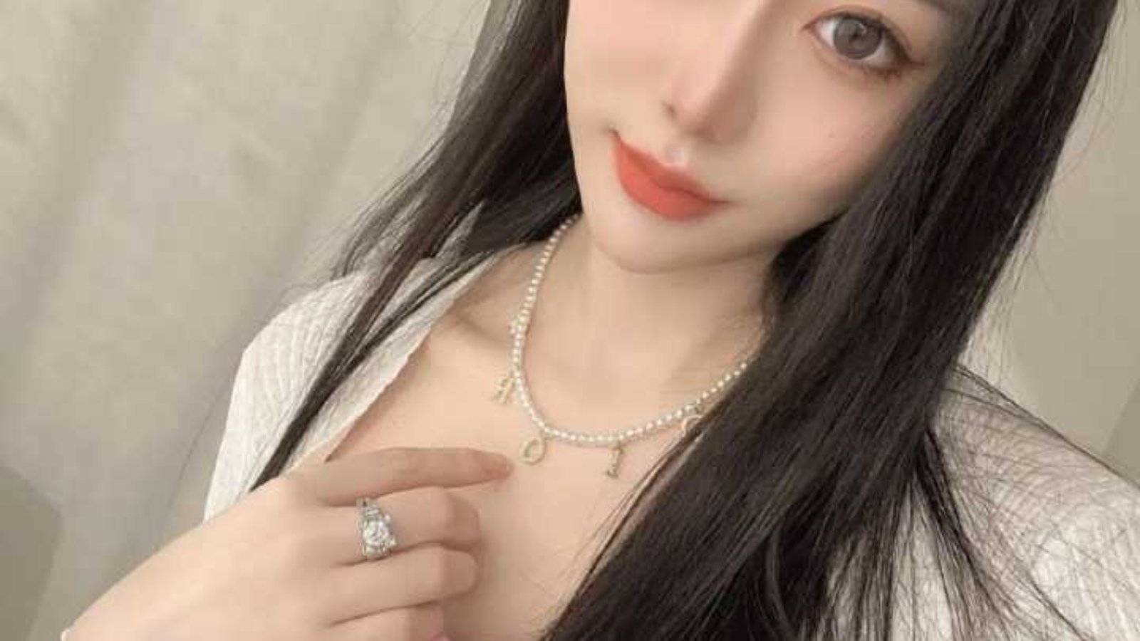 Portrait of a young woman with long dark hair wearing a pink top and a pearl necklace.