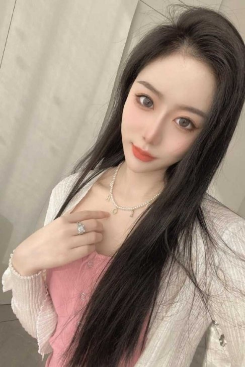 Portrait of a young woman with long dark hair wearing a pink top and a pearl necklace.