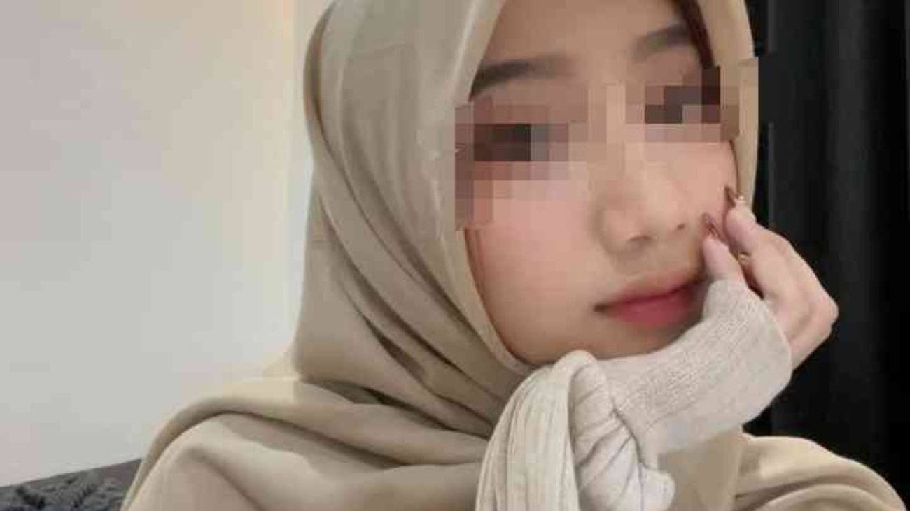 Kasya wearing a beige hijab and sweater, with hand on chin