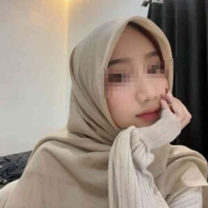 Kasya wearing a beige hijab and sweater, with hand on chin