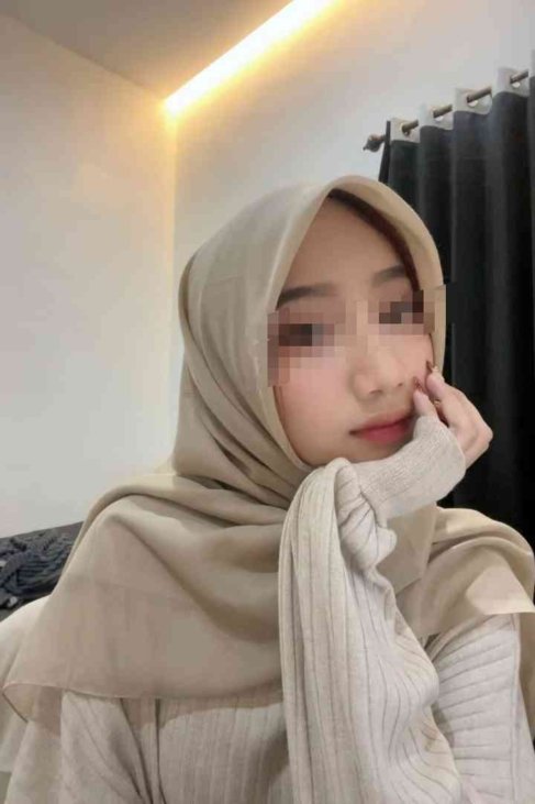 Kasya wearing a beige hijab and sweater, with hand on chin