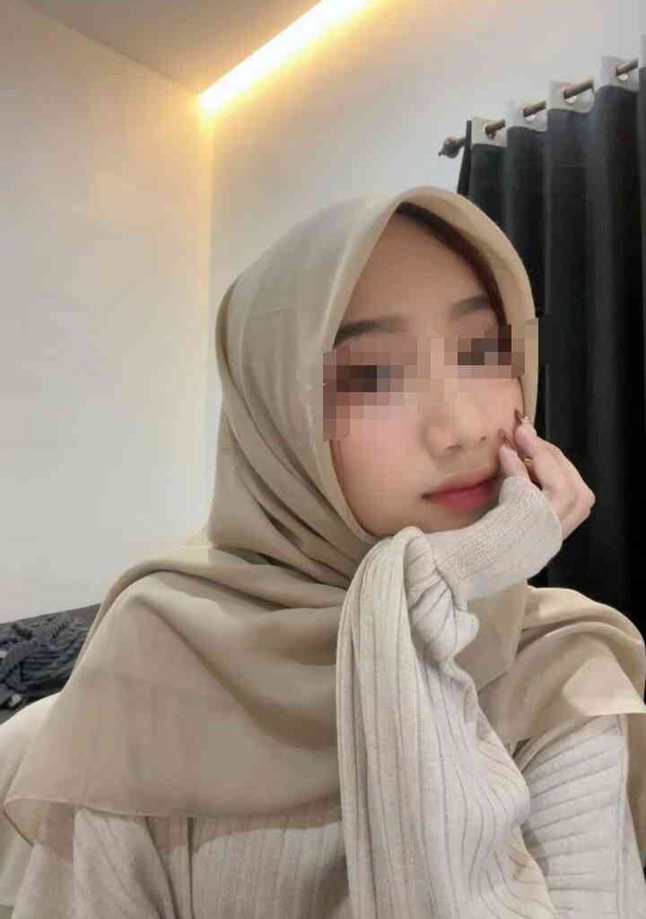 Kasya wearing a beige hijab and sweater, with hand on chin
